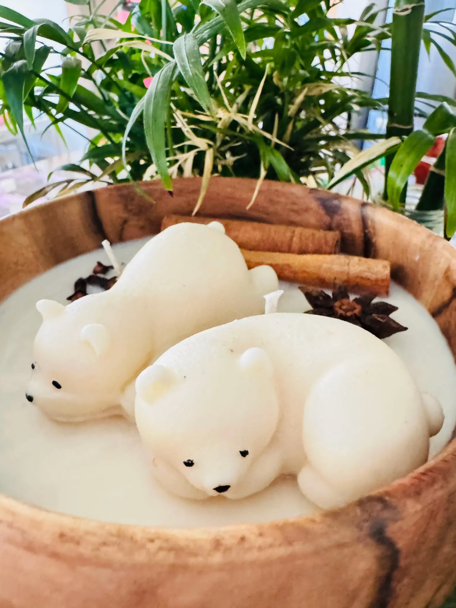 Close-up of two ivory polar bear figures with decorative spices in a wooden bowl candle